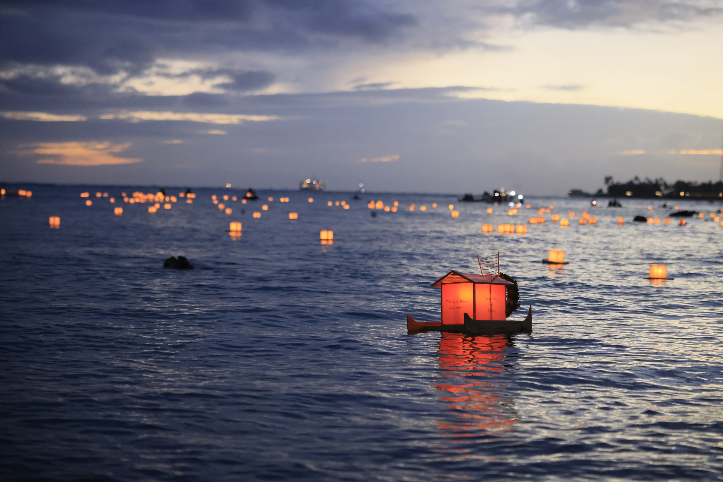 Glowing lanterns floating on the sea at dusk during Shinnyo Lantern Floating Hawaiʻi